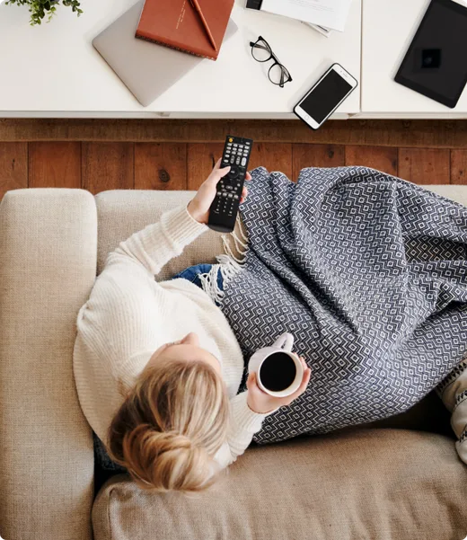 Person at home holding a television remote with a phone nearby